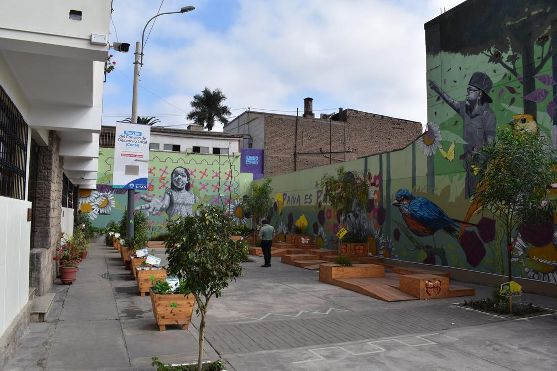 A pedestrian plaza with large murals, wooden play platforms and planters