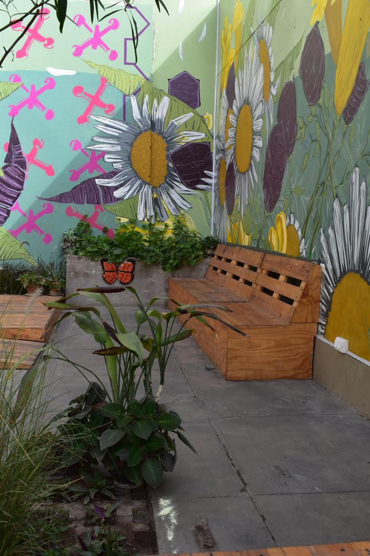 A wooden pallet bench beneath a painted daisy mural