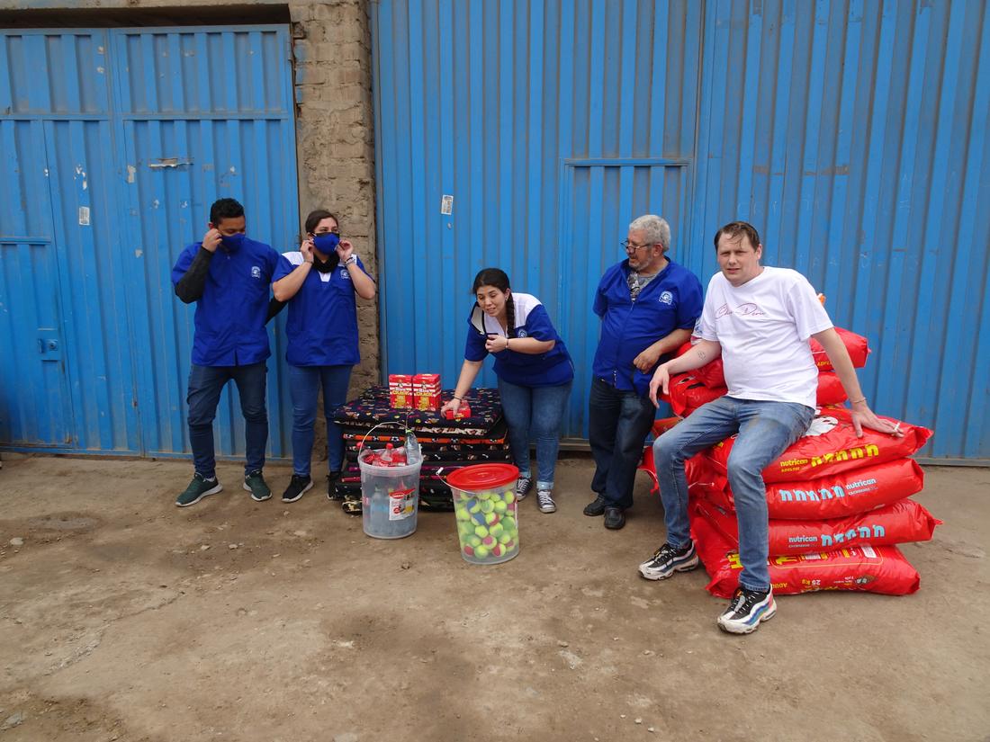 The team beside stacked food sacks, dog beds and a bucket of tennis balls